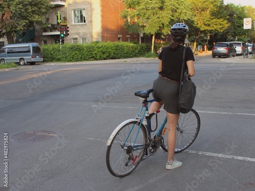 Young girl cycling in the urban neighborhood Plateau Mont Royal in Montreal, Quebec, Canada. Woman practices a healthy physical activity in summer on a city road, wearing a helmet.