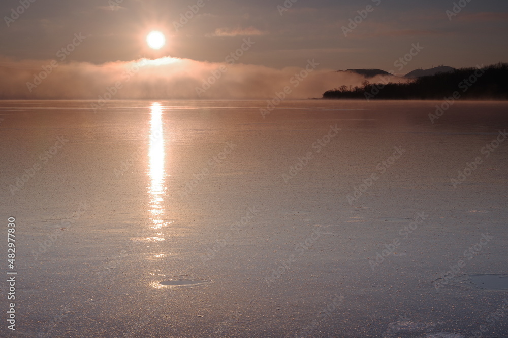 薄氷の湖面に輝く朝の太陽光。北海道の屈斜路湖。