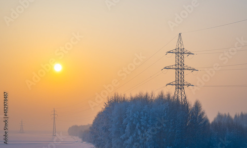 winter morning landscape of snow covered nature, trees and large poles of high voltage power transmission lines
