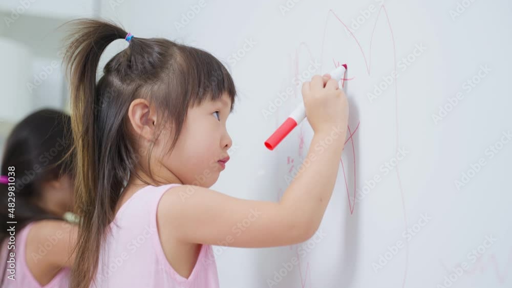 Asian young sibling kid girl enjoy paint on white wall in living room. Asian young sibling kid girl enjoy paint on white wall in living room.