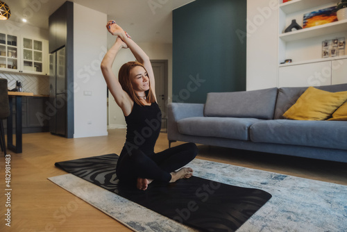 young woman with bright red hair trains on a rug in a modern apartment. slender muscular body of a woman. home independent training. selective focus, vertically photo