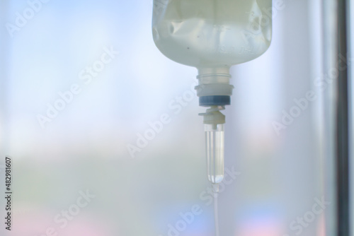 Closeup shot of clinical surgery injection infusion intravenous fluid liquid normal saline solution vial drip and plastic bag hanging on pole in patient ward room at hospital on blurred background
