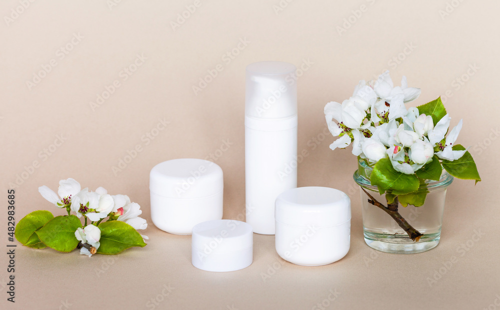 Anti-aging nourishing cosmetic products with apple extract on a beige pastel background, spring apple tree flowers nearby. Presentation of cosmetics for face and body care with fruit extracts Anti-aging nourishing cosmetic products with apple extract on a beige pastel background, spring apple tree flowers nearby. Presentation of cosmetics for face and body care with fruit extracts