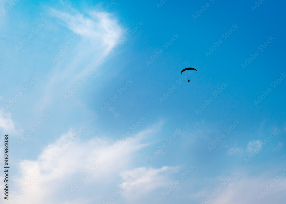 Parachutist soaring in a beautiful blue sky with light clouds. Paraglider - Feeling free on the sky