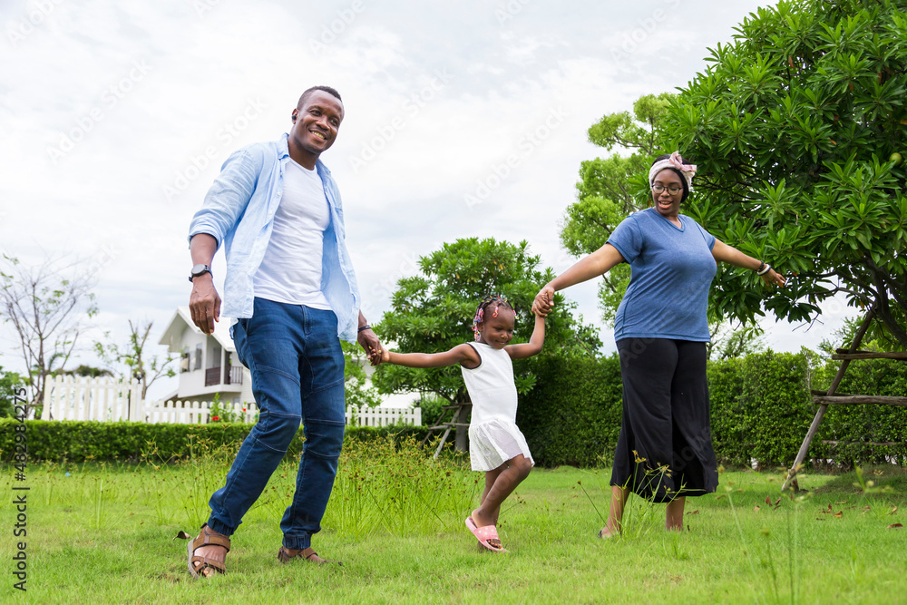 Happy family of African American people with young little daughter walking on green grass field while enjoying summer garden outside the house in the neighborhood