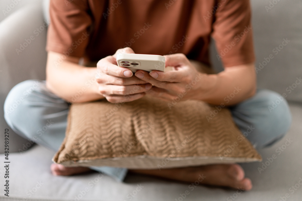 Technology Concept The man sitting next to a pot of plant, putting a small pillow on his lap, and checking something on his smartphone Technology Concept The man sitting next to a pot of plant, putting a small pillow on his lap, and checking something on his smartphone