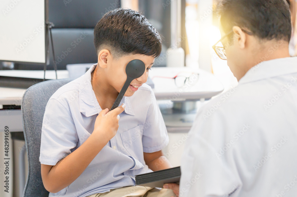 Fototapeta premium Smiling Indian boy doing eye test checking examination with optometrist in optical store