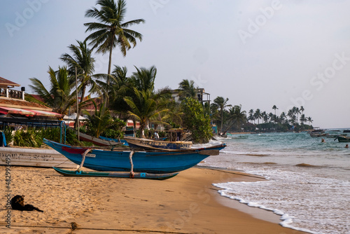 Boat on the sand beach with palms and ocean waves.