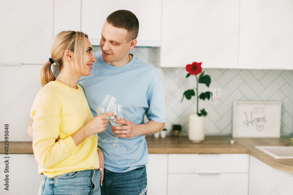 A romantic young couple holding a glass, standing in a modern kitchen, celebrating an anniversary or Valentine's Day together