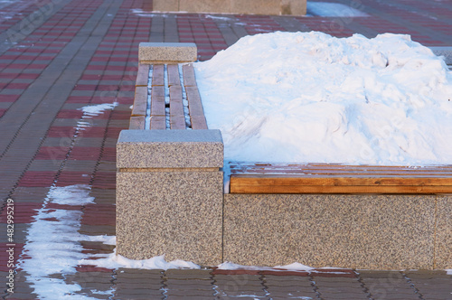 A bench with a flower bed in winter, filled with a snowdrift. Promenade of the city embankment.