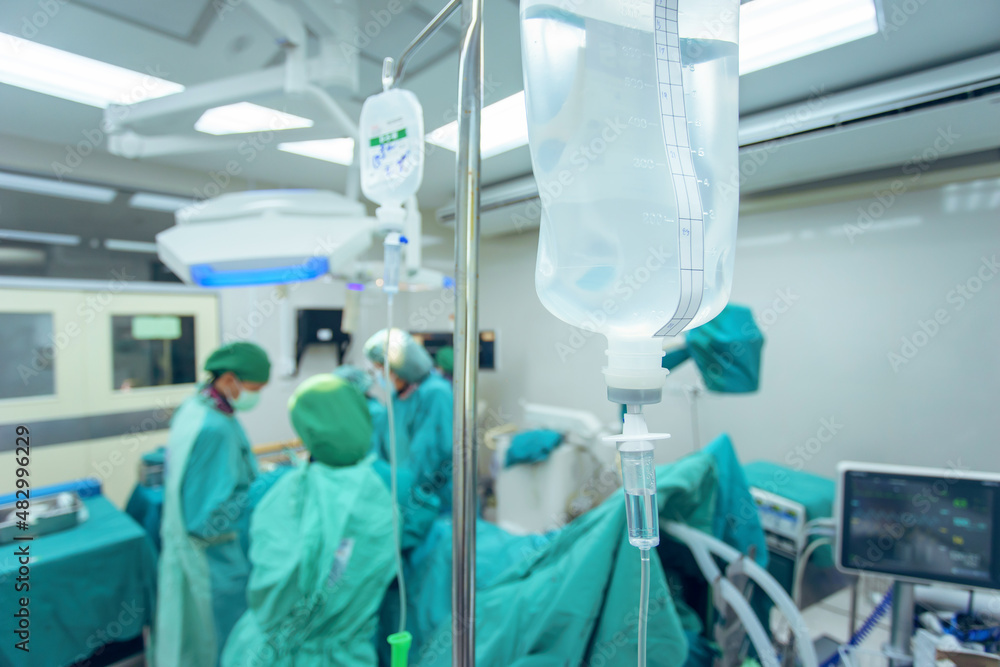 Selective focus on drip system and saline bag with surgical team in operation room on a blurred background. Selective focus on drip system and saline bag with surgical team in operation room on a blurred background.
