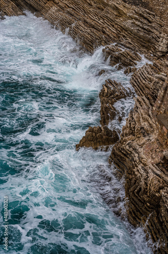 Dramatic marine background. Rocky coast of Adriatic Sea. White foamy waves beat against stone shore. Panorama of sea coast. Aerial top view.
