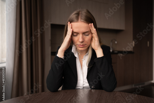 Unhealthy caucasian female freelancer with touch head massage suffering from migraine at home workplace. Dizziness or headache. Sick young employee