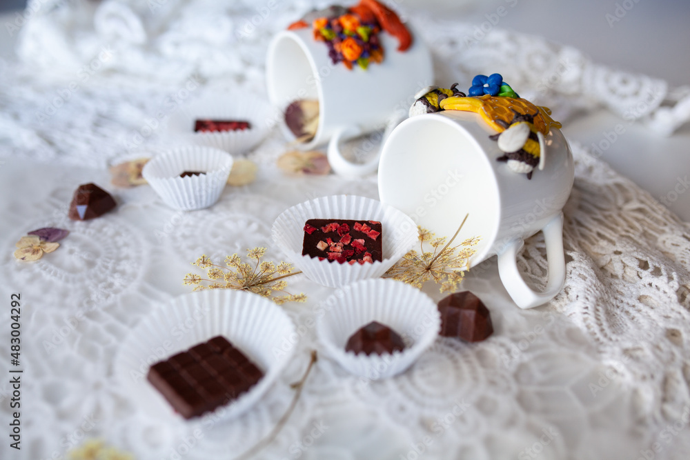 White mugs and saucers with handmade chocolate on a lace background White mugs and saucers with handmade chocolate on a lace background