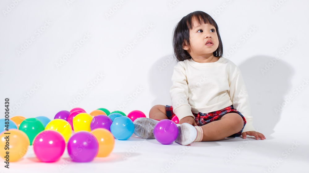 Studio shot of little cute short black hair Asian baby girl daughter model in casual plaid skirt sitting on floor smiling laughing playing with colorful round balls toy alone on white background Studio shot of little cute short black hair Asian baby girl daughter model in casual plaid skirt sitting on floor smiling laughing playing with colorful round balls toy alone on white background