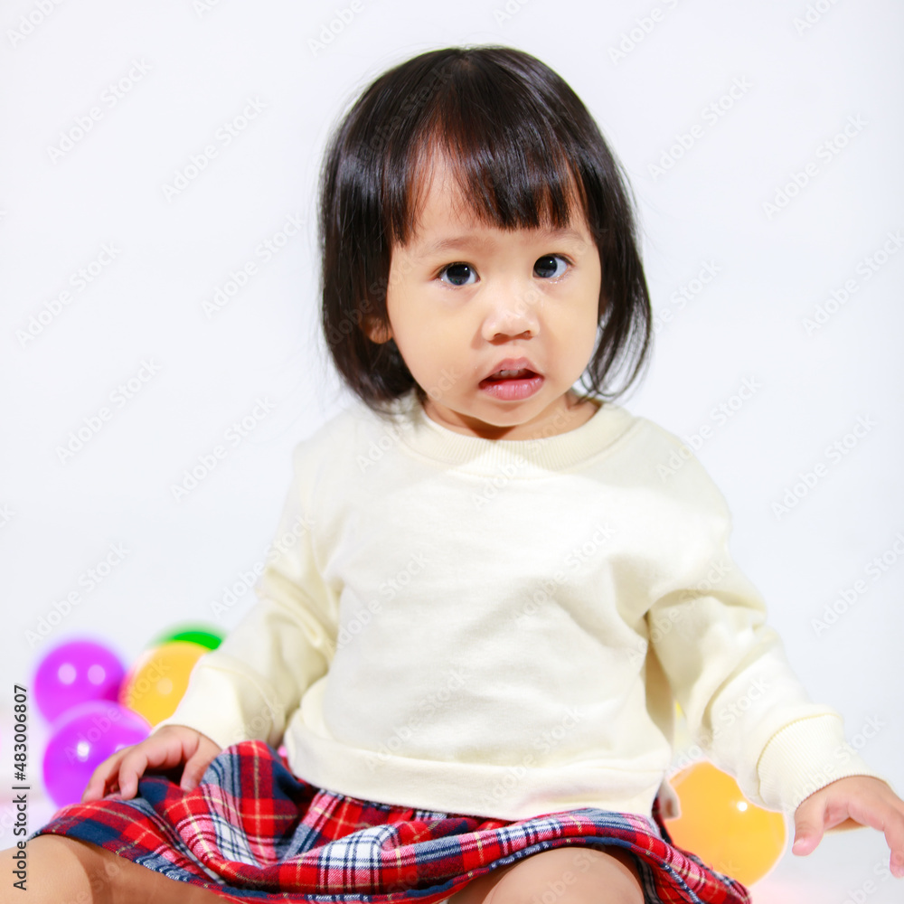 Studio shot of little cute short black hair Asian baby girl daughter model in casual plaid skirt sitting on floor smiling laughing playing with colorful round balls toy alone on white background Studio shot of little cute short black hair Asian baby girl daughter model in casual plaid skirt sitting on floor smiling laughing playing with colorful round balls toy alone on white background
