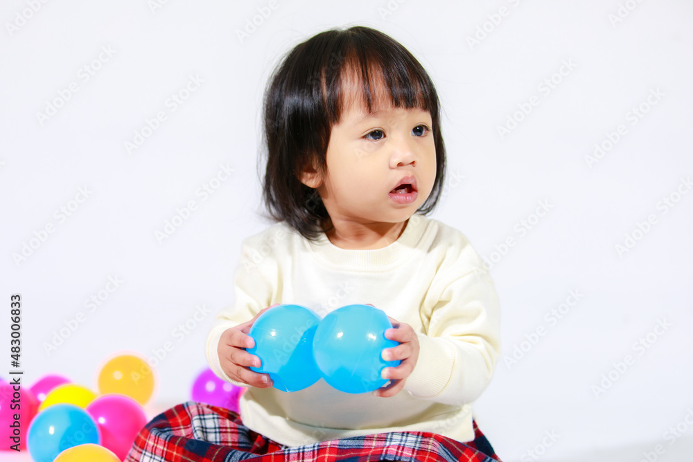 Studio shot of little cute short black hair Asian baby girl daughter model in casual plaid skirt sitting on floor smiling laughing playing with colorful round balls toy alone on white background Studio shot of little cute short black hair Asian baby girl daughter model in casual plaid skirt sitting on floor smiling laughing playing with colorful round balls toy alone on white background