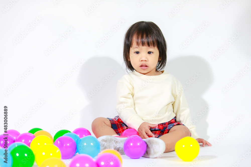 Studio shot of little cute short black hair Asian baby girl daughter model in casual plaid skirt sitting on floor smiling laughing playing with colorful round balls toy alone on white background Studio shot of little cute short black hair Asian baby girl daughter model in casual plaid skirt sitting on floor smiling laughing playing with colorful round balls toy alone on white background