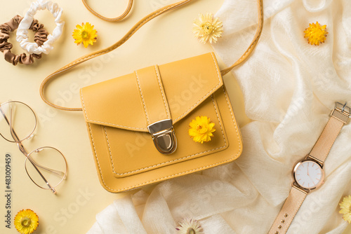 Top view photo of woman's day composition yellow leather handbag stylish glasses scrunchies golden wrist watch and field flowers on isolated beige background photo