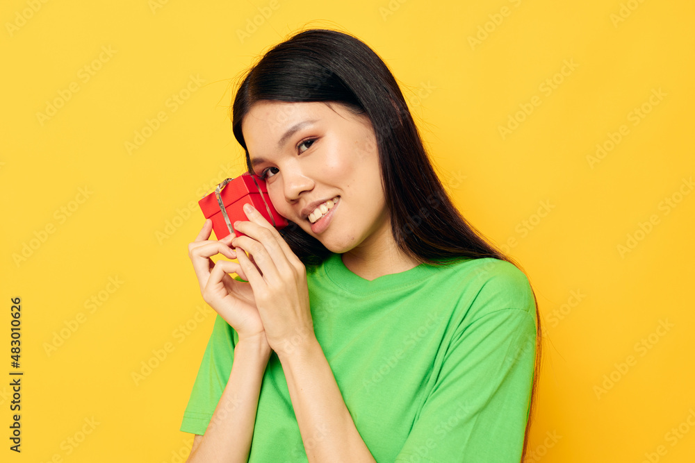 woman with Asian appearance in green T-shirts with a small gift box yellow background unaltered woman with Asian appearance in green T-shirts with a small gift box yellow background unaltered