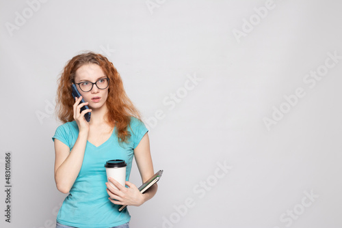 a girl in a blue T-shirt with a phone and coffee on a light background
