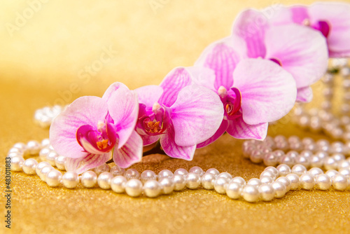 purple Orchid and pearl necklace on a shiny gold background 