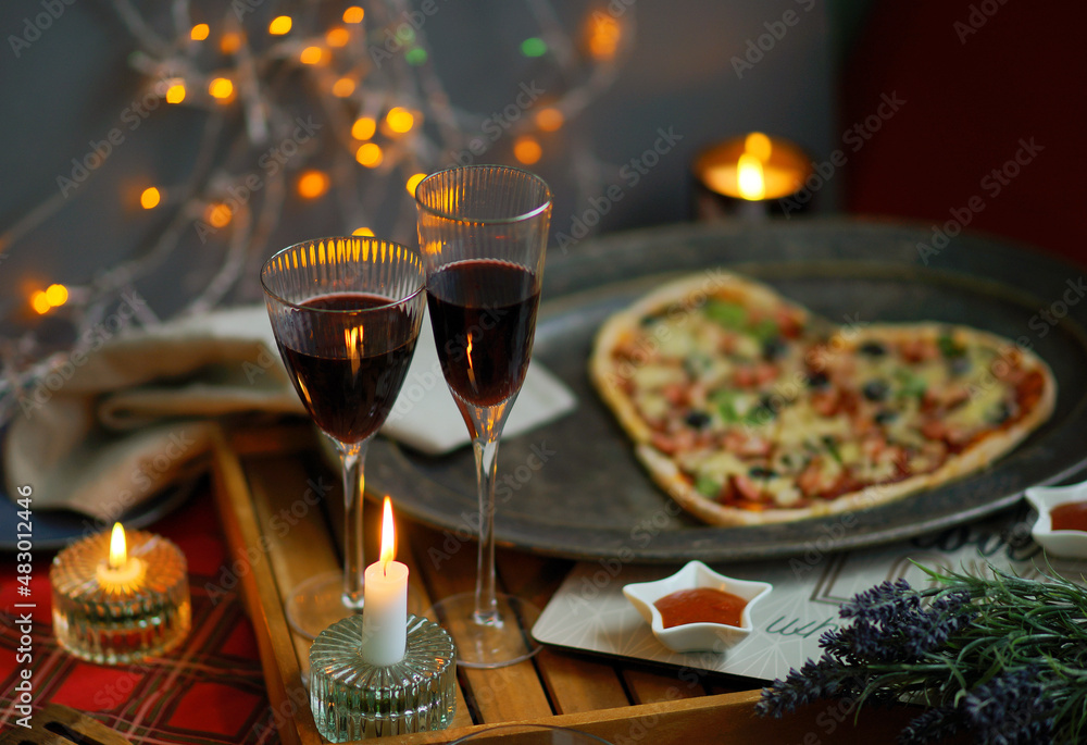 Romantic table setting. Evening for st Valentin's Day celebration. Heart shaped Pizza, lights, glass of champagne. 