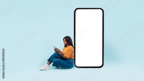 Black woman leaning on white empty smartphone screen, using cellphone
