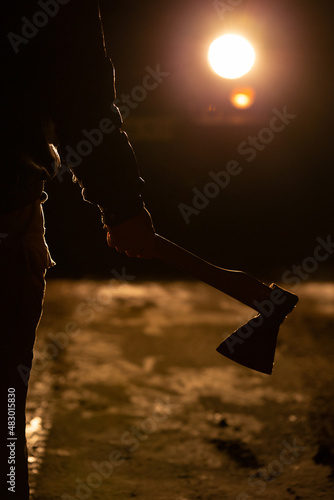 Man stands on the road at night and holds an ax in his hand