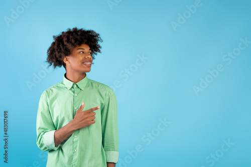 Look at this. Excited african american student guy pointing and looking aside at empty space over blue background