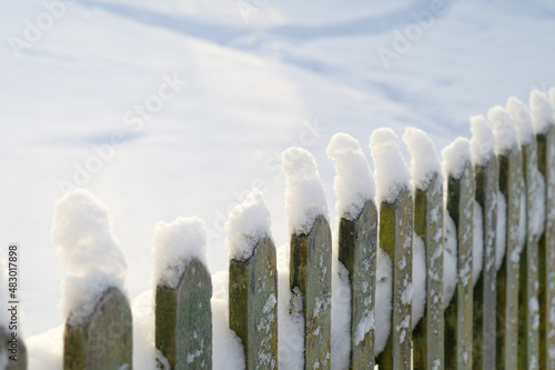 Snow-covered old fence, caps of snow on the fence