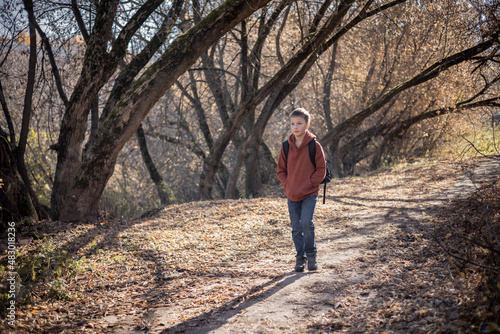 Teenager boy with backpack walking on path in autumn park. Active lifestyle, Back to school. Student boy in fall forest. © Lyubov