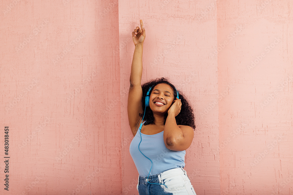 Happy woman wearing blue headphones leaning on a wall and smiling Happy woman wearing blue headphones leaning on a wall and smiling