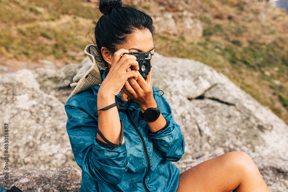 Young female taking photographs of the landscape with a film camera. Woman use a small camera while taking a break during hiking. Young female taking photographs of the landscape with a film camera. Woman use a small camera while taking a break during hiking.