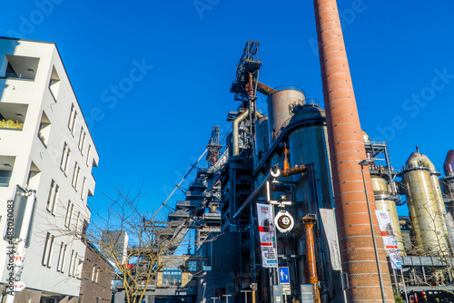 A low angle shot of an old reconverted steel tower chimney and modern buildings photo