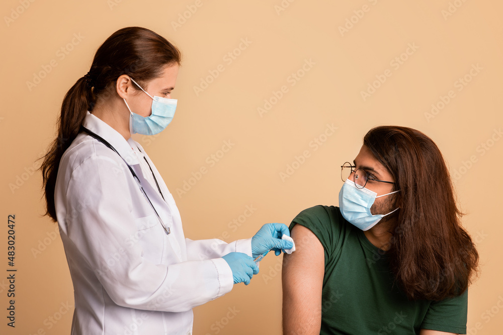 Friendly woman doctor in face mask disinfecting skin before injection