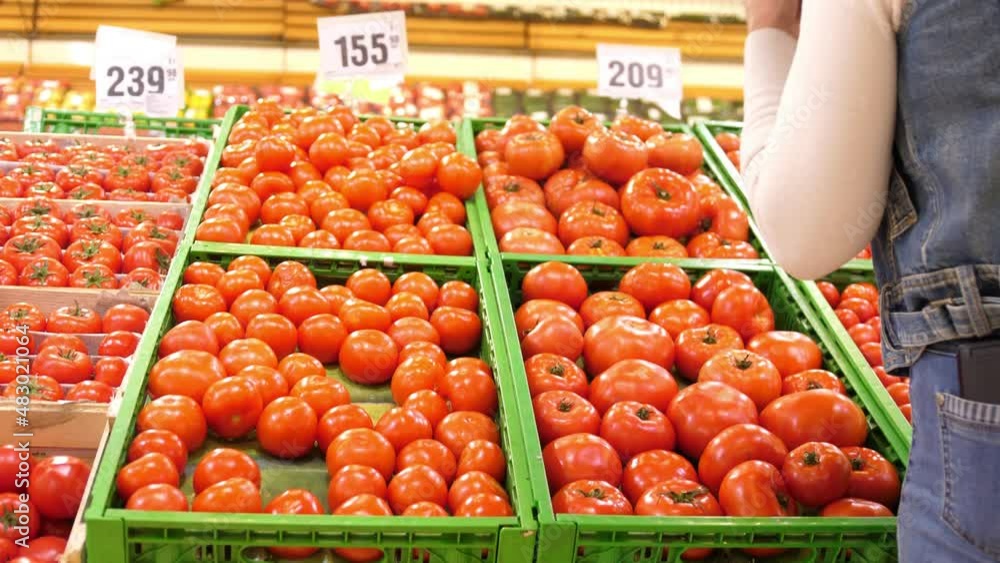 A woman chooses and buys tomatoes in supermarket A woman chooses and buys tomatoes in supermarket