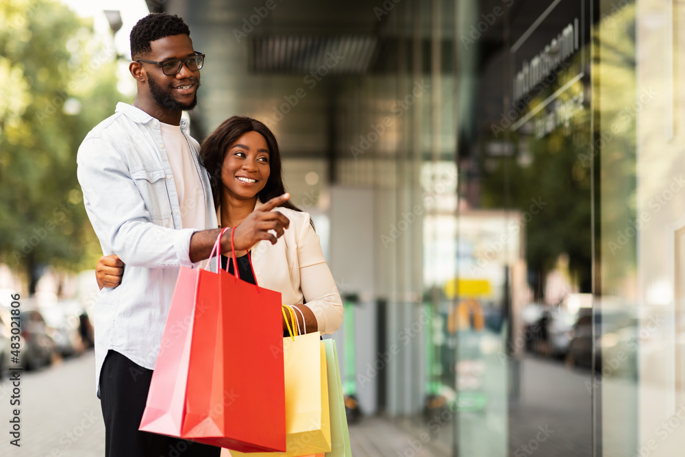 Portrait of black couple with shopping bags pointing at window Portrait of black couple with shopping bags pointing at window