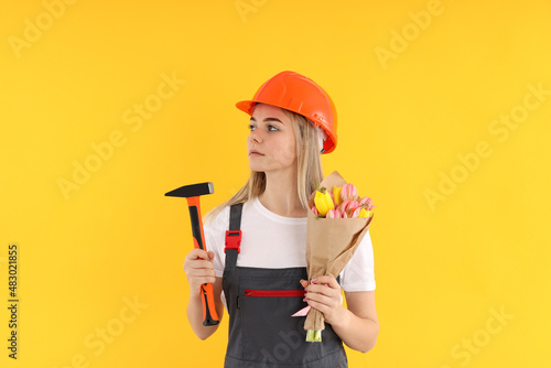 Builder girl with bouquet of flowers on yellow background © Atlas