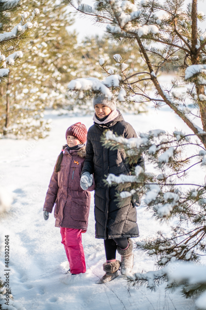 Fototapeta premium Mother and daughter are walking in the winter forest. Winter trip with family in the forest.