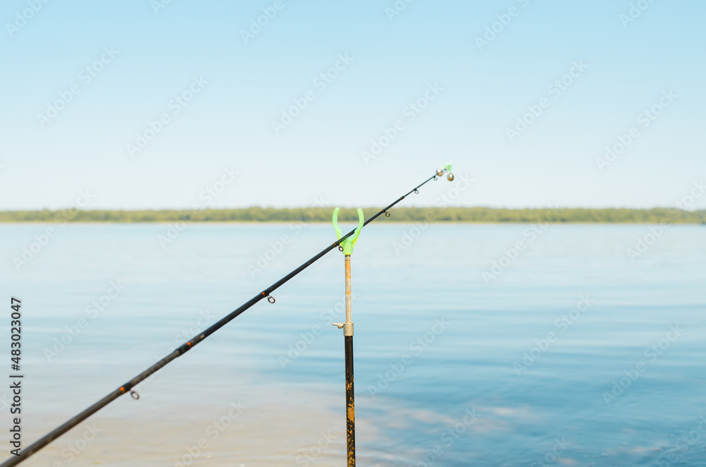 Close-up of fishing rod with bell on stand on lake outdoors. Summer fishing. Selective focus