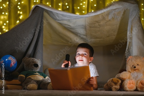 boy reading book with flashlight in tent at night