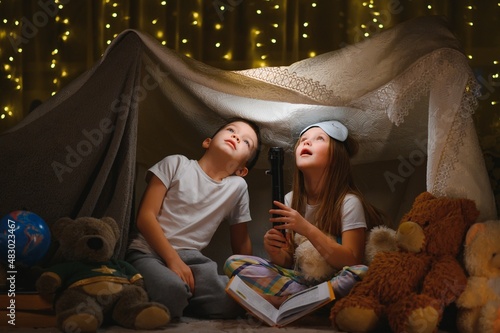 Photographie Two little child play at home in the evening to build a camping tent to read books with a flashlight and sleep inside