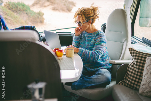 Foto Adult nice woman work on laptop sitting in a camper van dinette enjoying freedom travel vacation or vanlife lifestyle