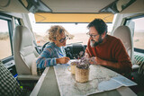 Adult couple planning next travel destination sitting inside a camper van using a paper map guide on the table. ature traveler and vanlife alternative people lifestyle. Couple of tourist and beach
