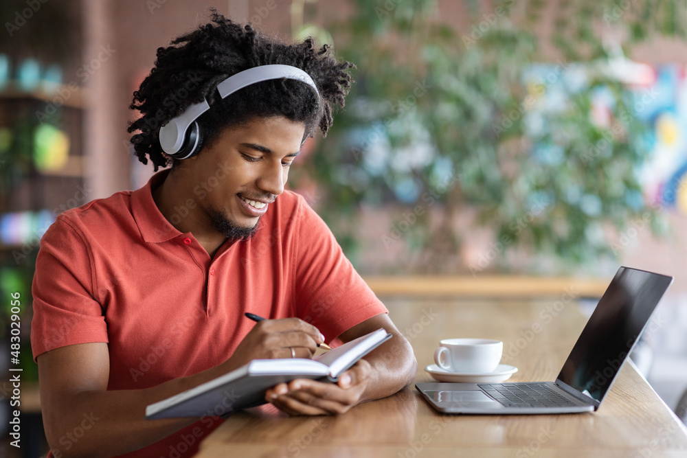 Young Black Guy Taking Notes While Studying Online With Laptop In Cafe Young Black Guy Taking Notes While Studying Online With Laptop In Cafe