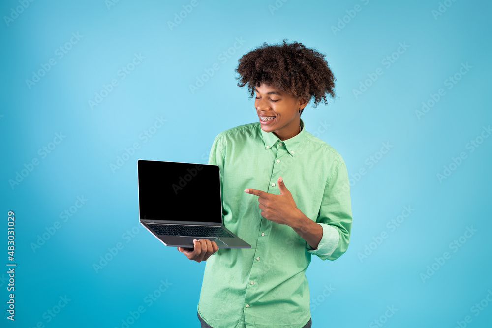 Great website. Teen african american guy showing laptop computer blank screen, standing over blue background Great website. Teen african american guy showing laptop computer blank screen, standing over blue background