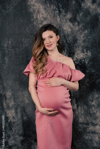 Pregnant woman in pink dress touching belly
