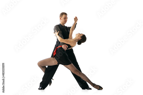 Beautiful sportive young man and woman dancing Argentine tango isolated on white studio background. Artists in black stage costumes