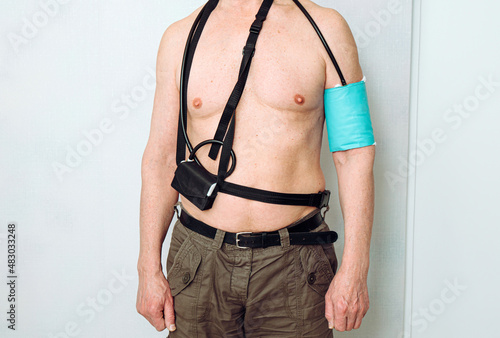 Body of a middle aged man using portable Ambulatory Blood Pressure Monitor (ABPM) for taking measurements during normal daily activities at home.